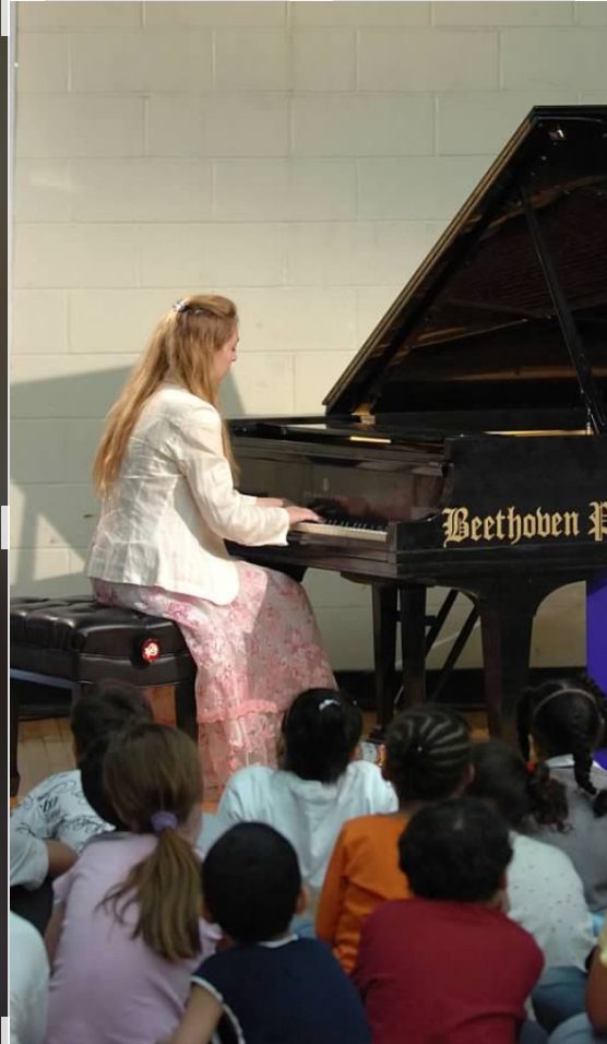 Children seated together watching Katya Grineva perform at a grand piano